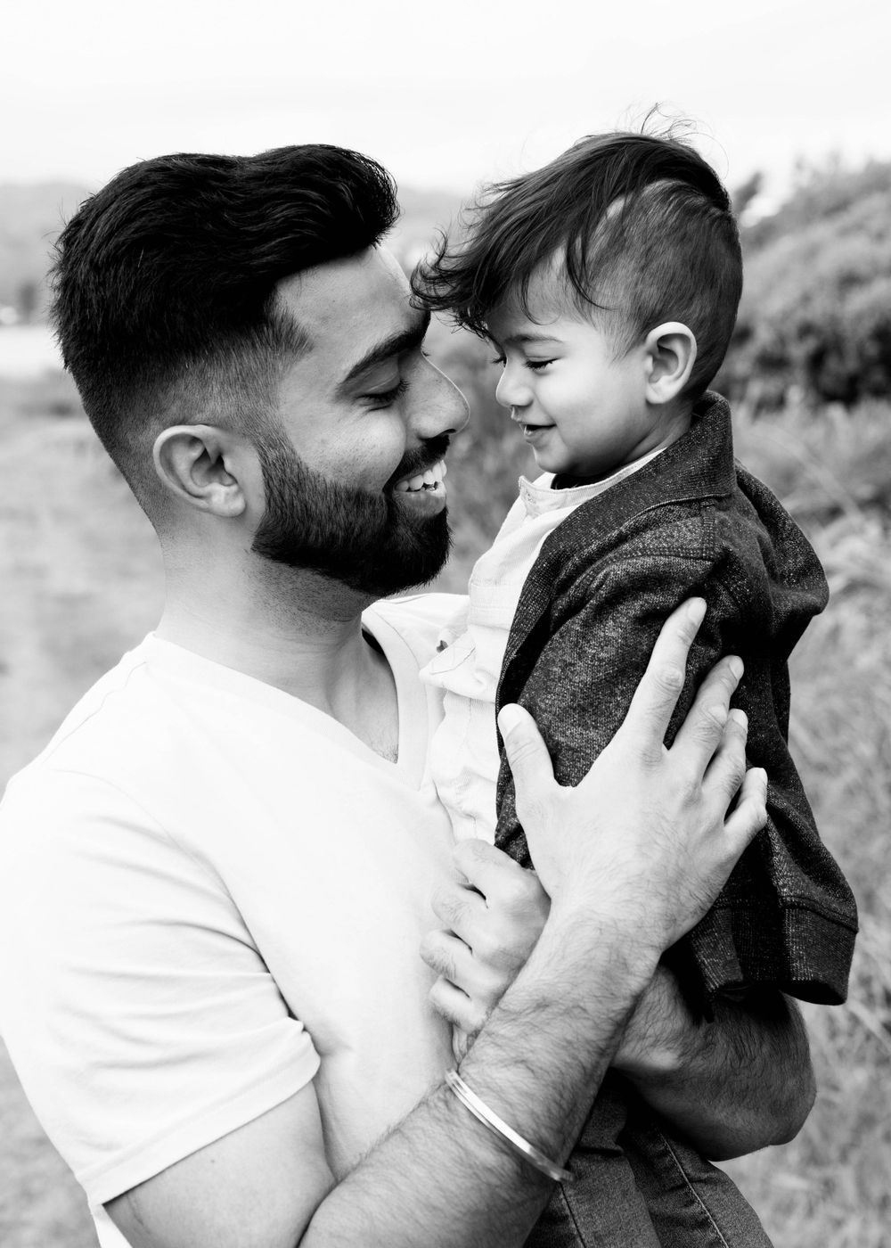 Black and white portrait of boy and his father on the beach smiling at each other.
