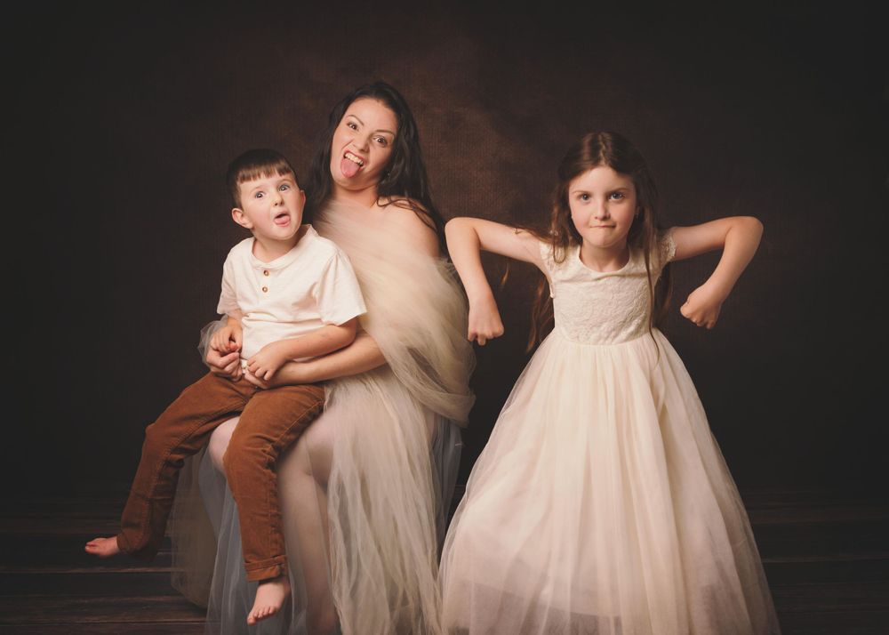Family portrait of mother, daughter and son being silly on a brown backdrop.