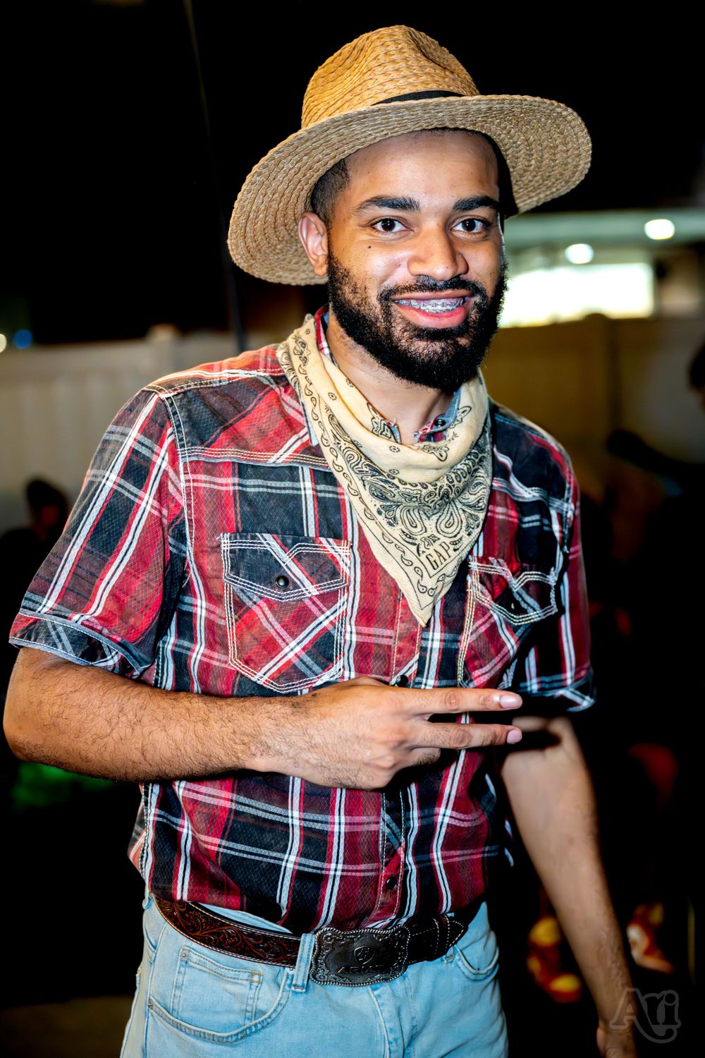 Person in western attire with plaid shirt and straw hat at a nighttime event.