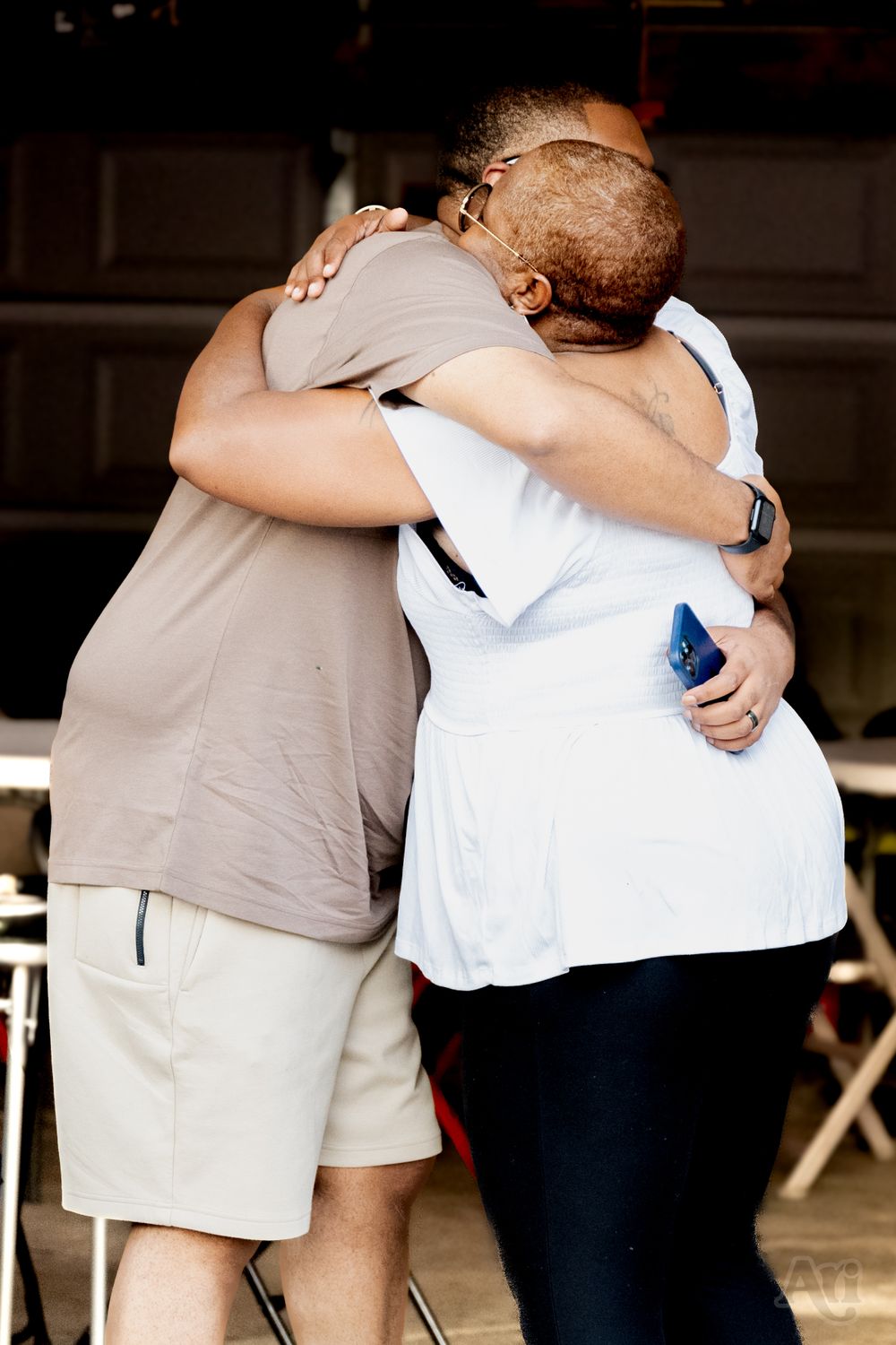 Two people share an emotional embrace at an outdoor event wearing casual summer attire.