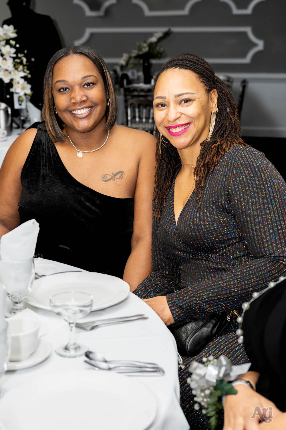 Two people smiling while seated at formal dining table with white tablecloth and place settings.