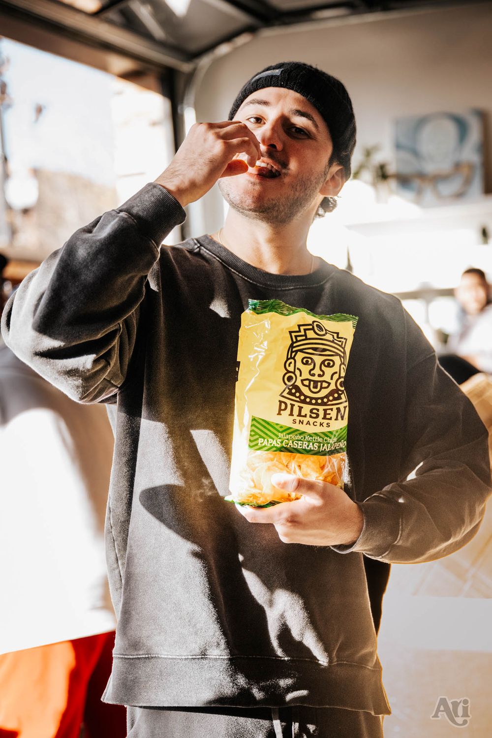 Person in casual wear enjoying snacks from a bag in an industrial-style setting.