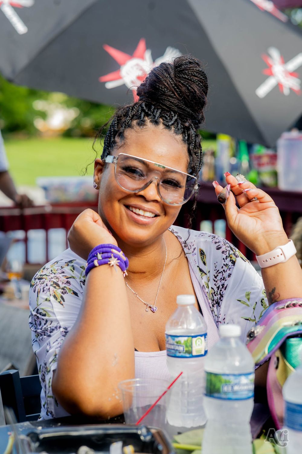 Person with braided updo and clear glasses smiles at outdoor party under decorative umbrellas.