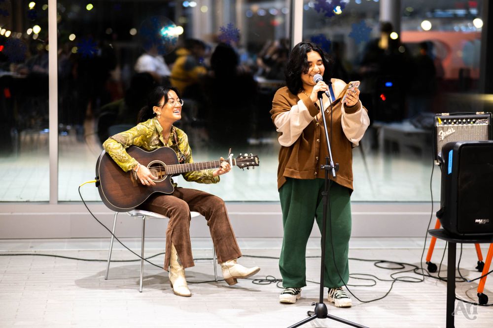 Two musicians perform on stage, one playing guitar while other sings into microphone.