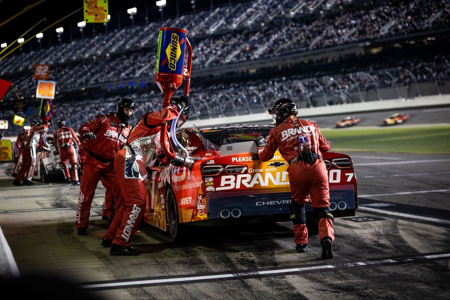 NASCAR pit crew services a red Chevy race car at night during a Daytona race, with crew members in matching uniforms.