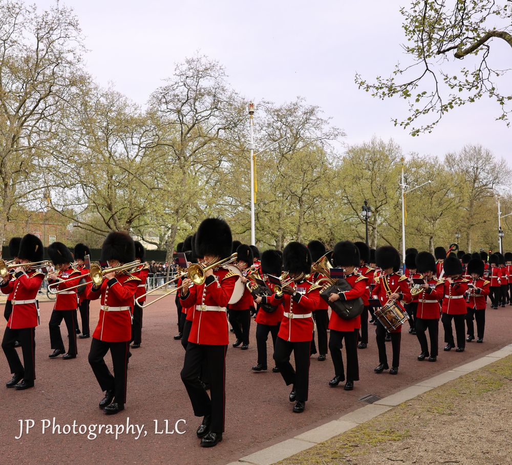 Military band in red uniforms performs in formation during an outdoor ceremony.