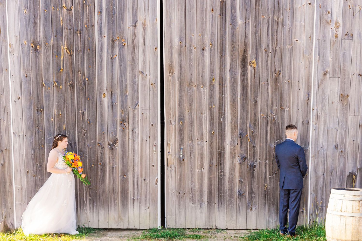 Rustic barn wedding first look moment with couple on opposite sides of wooden door.