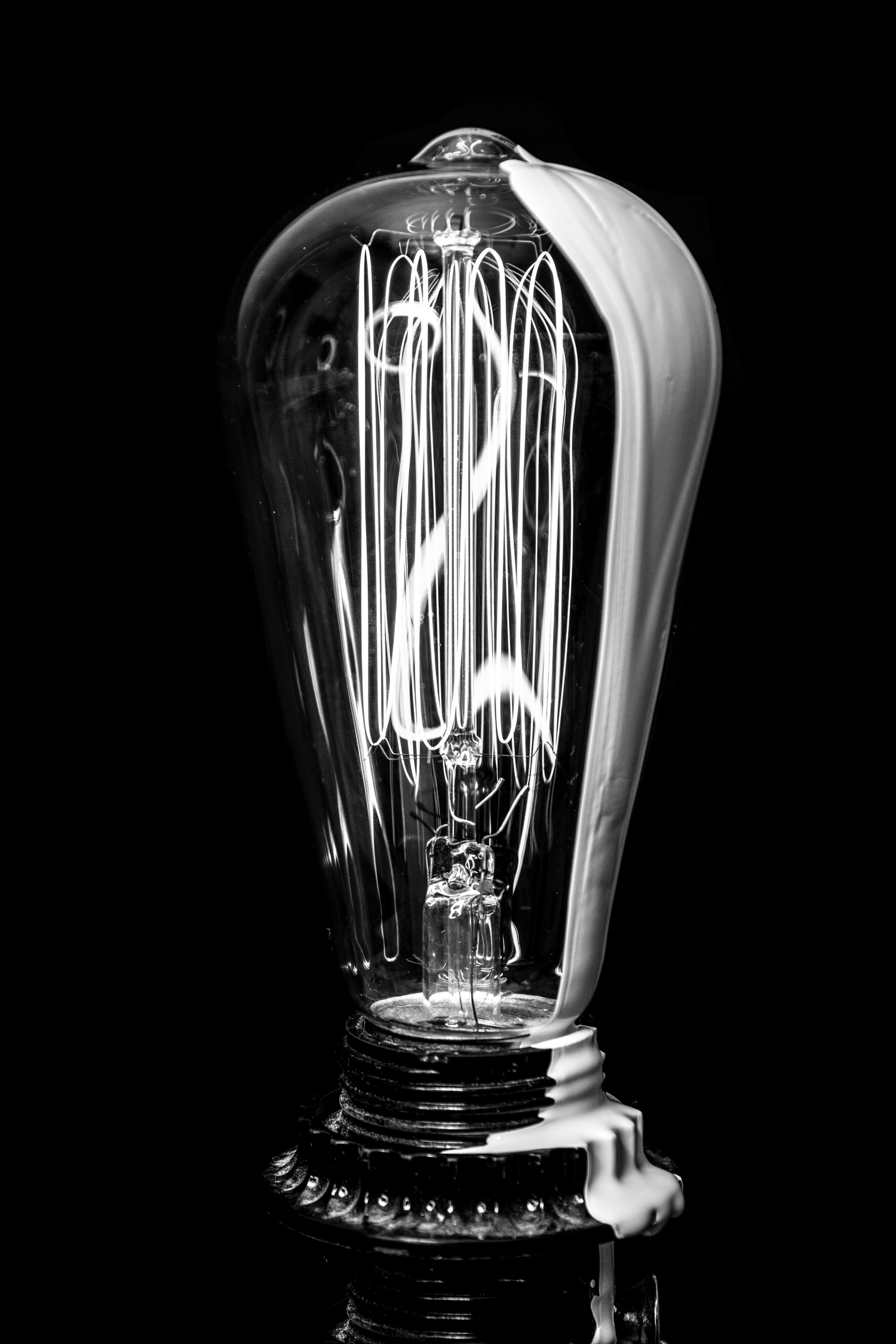 Vintage Edison light bulb with glowing filament against black background in monochrome.