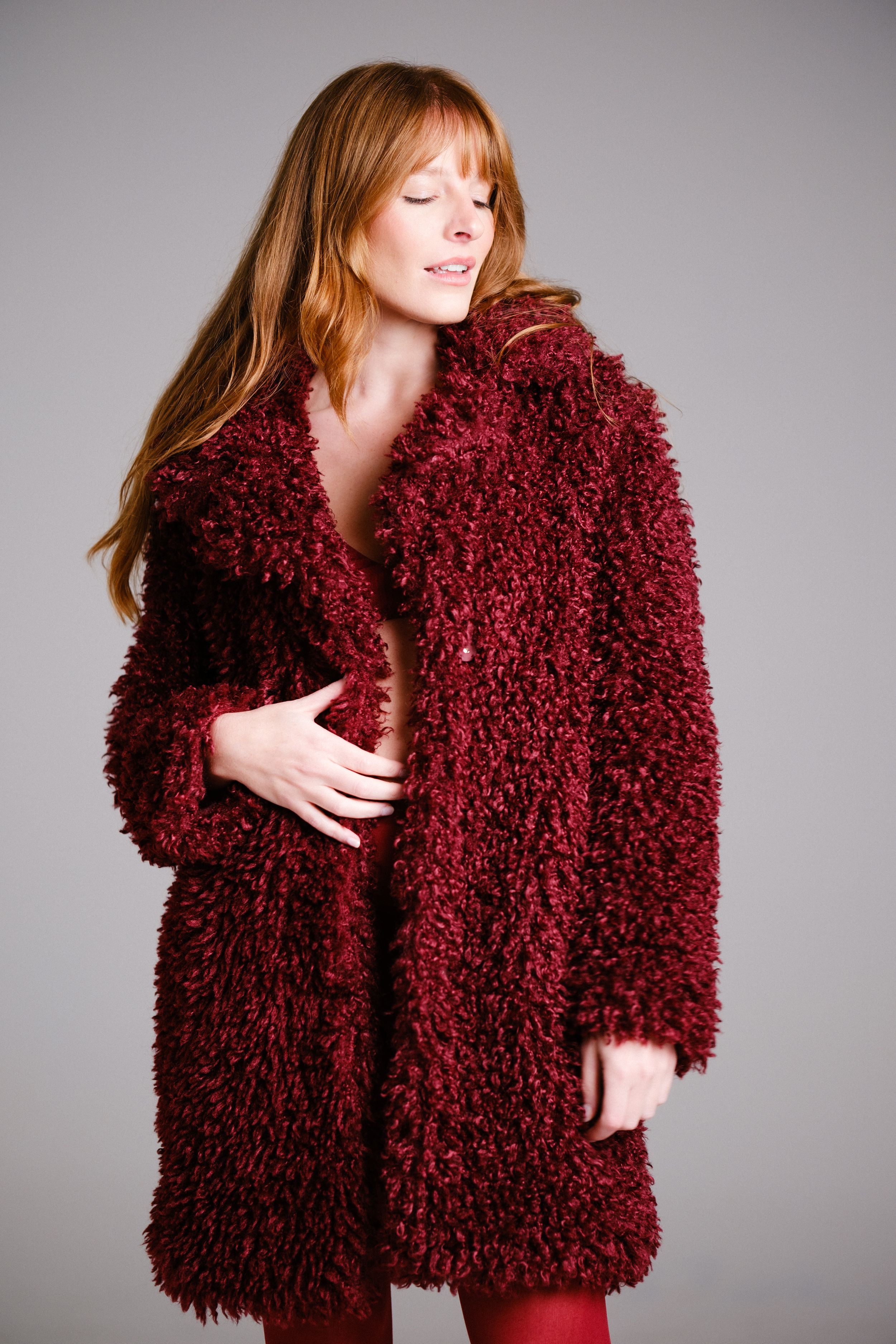 Model showcases plush burgundy coat in artistic fashion poses.