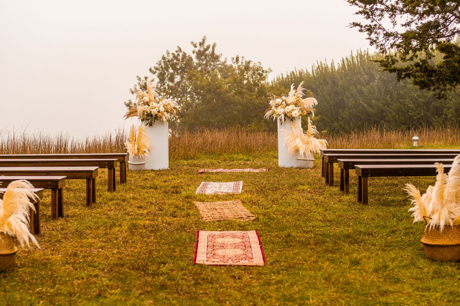 Rustic outdoor wedding ceremony setup with wooden benches and boho decor at sunset.