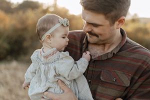 Heartwarming close-up of father holding baby in plaid shirt against sunset backdrop.