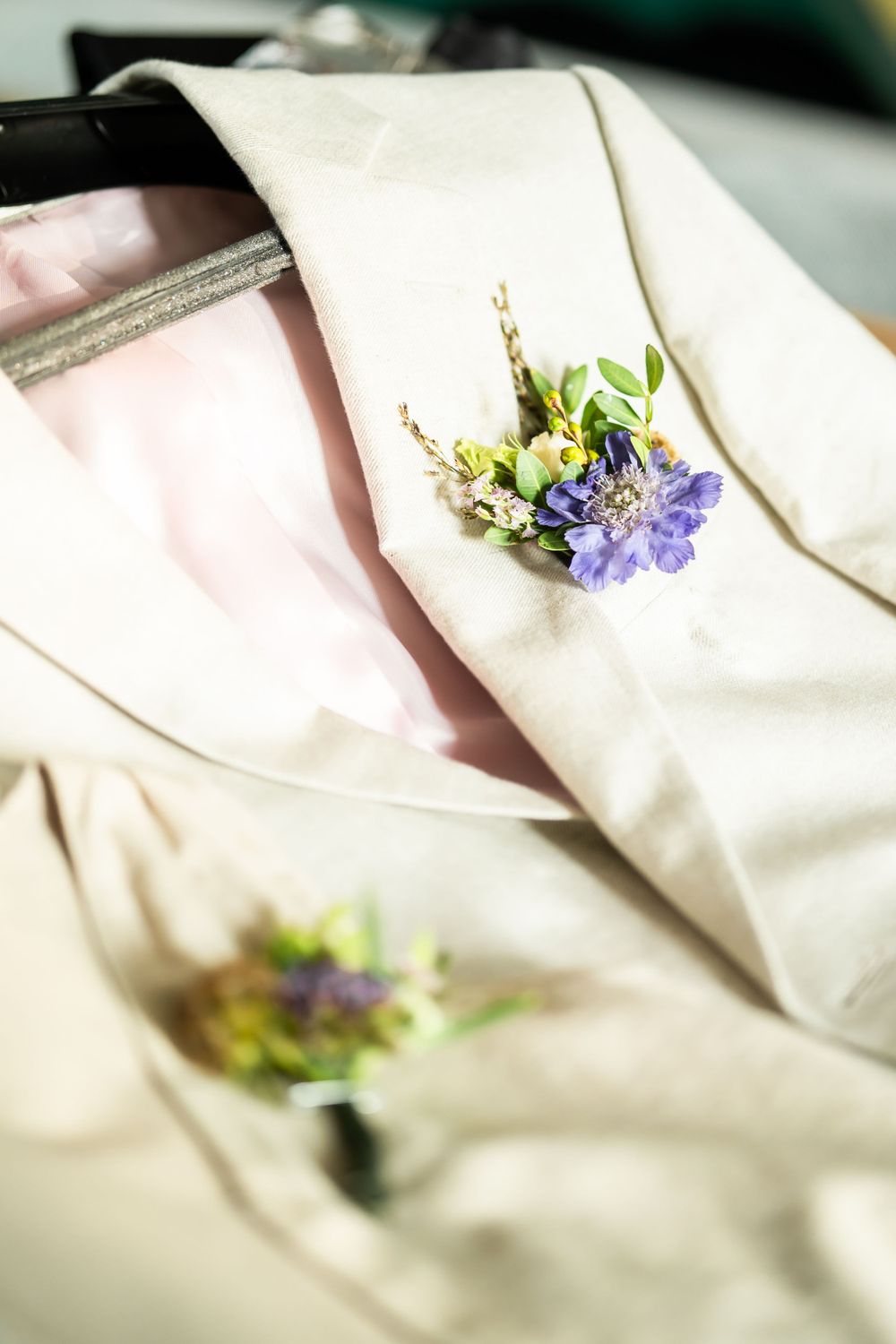 A delicate purple and yellow floral boutonniere rests on a cream colored suit jacket lapel.