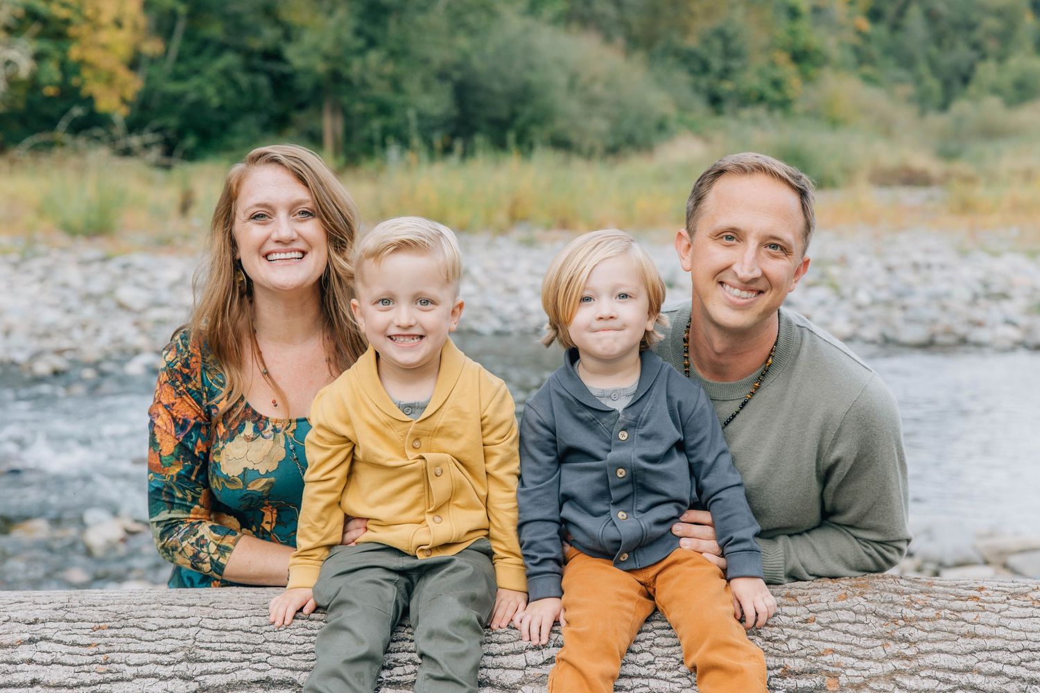Happy family of four sitting on a log near a river during fall family portraits.