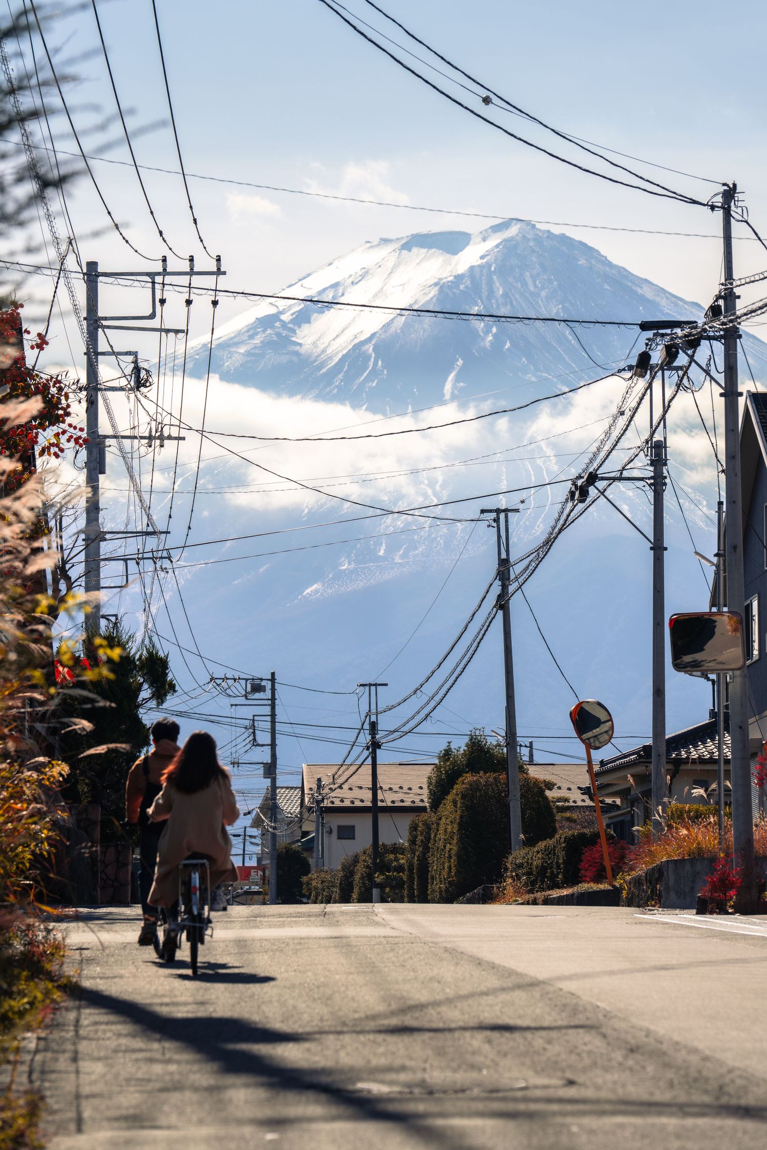 Snow-capped Mount Fuji towers in the distance behind power lines and a residential street in Japan.