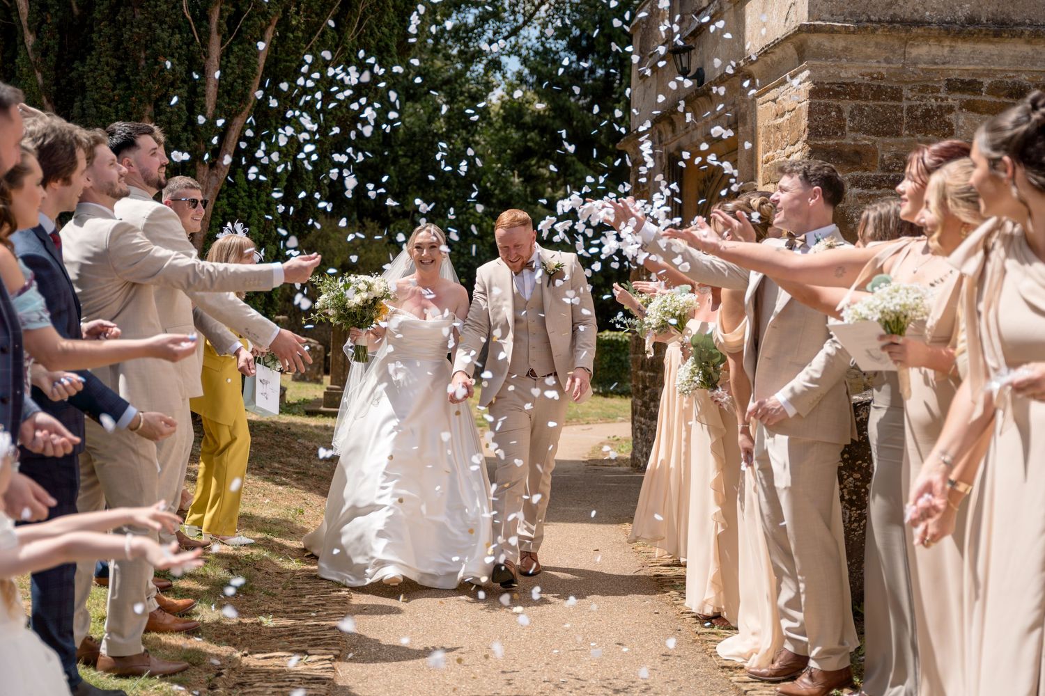 A bride and groom with their little boy and French bull dog in an open field with trees. The bride and from are crouched down.