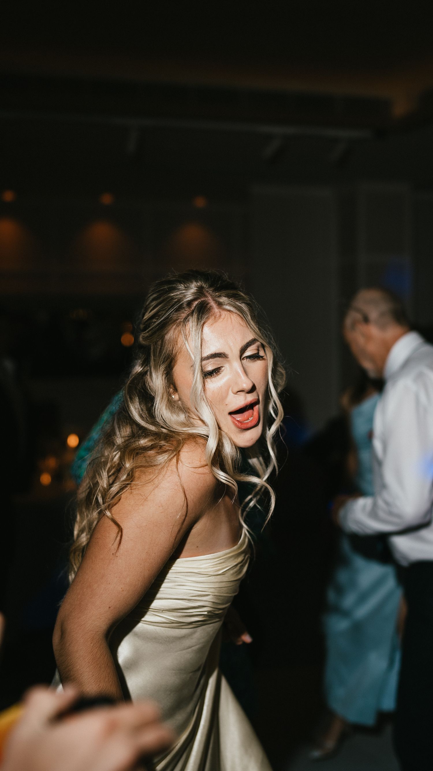 A joyful person in a white dress dances and laughs during a wedding reception.