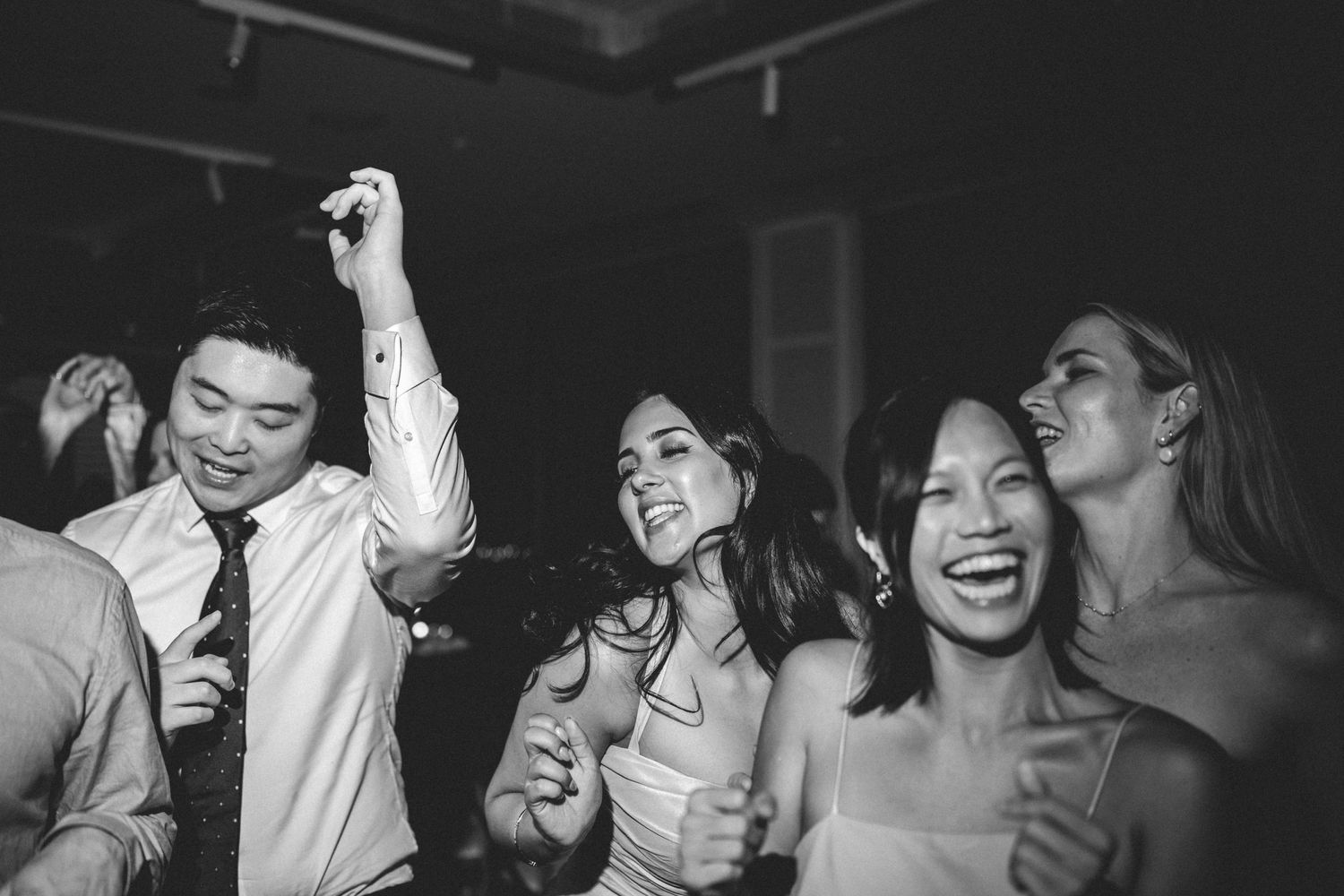 Wedding party guests dancing and singing together at a lively reception celebration in black and white.