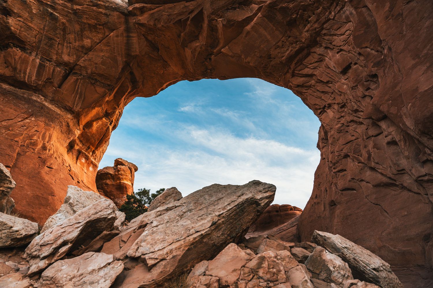 Natural rock arch formation in red sandstone revealing blue sky through the opening in desert landscape.