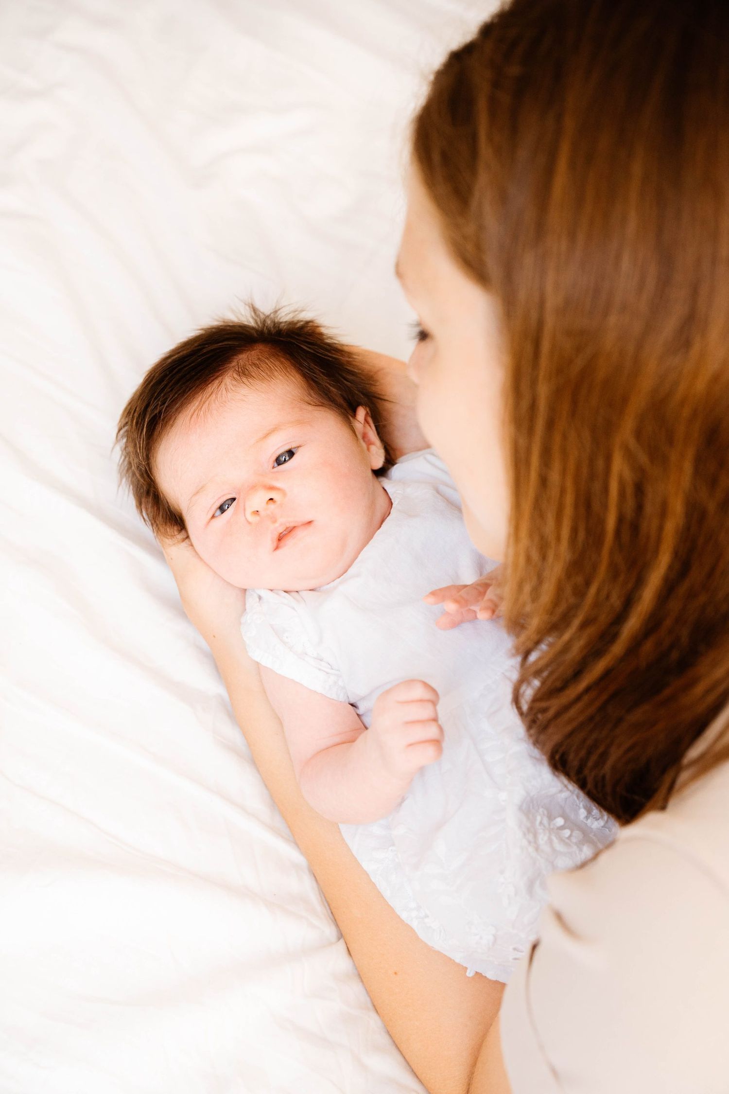 Intimate portrait of baby in white clothing on soft bedding.
