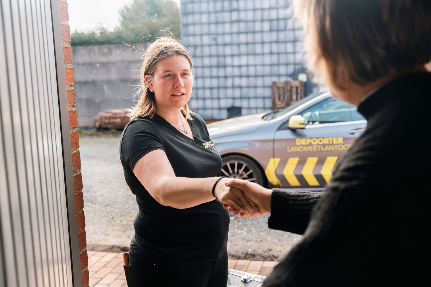 Professional in black uniform meeting client outside industrial building.