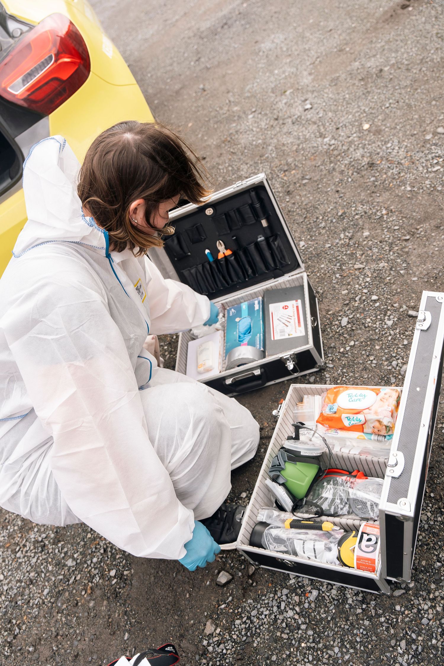 Person in protective white suit examining contents of equipment cases on ground.