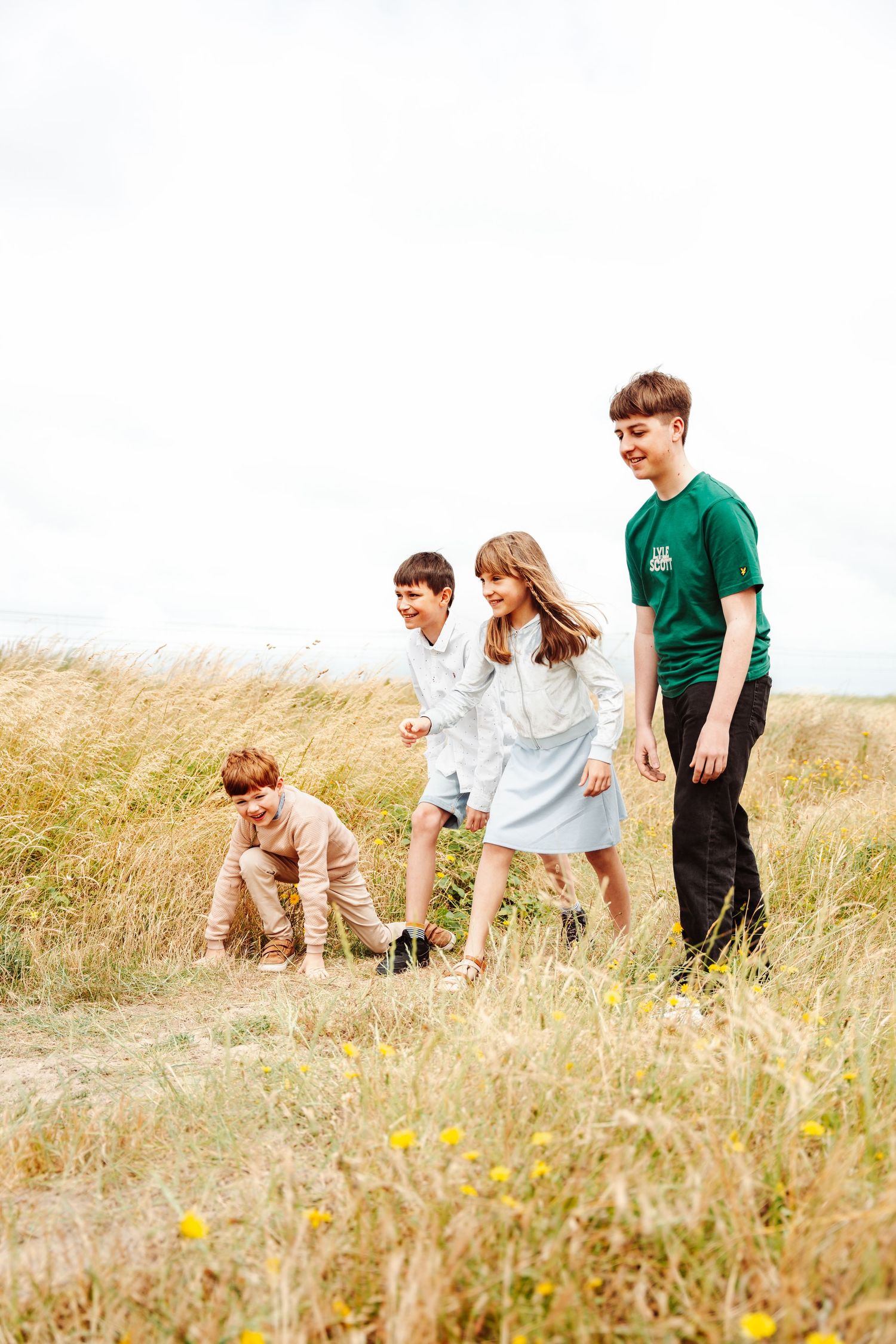 Young people playing and walking through tall grass in a coastal field.
