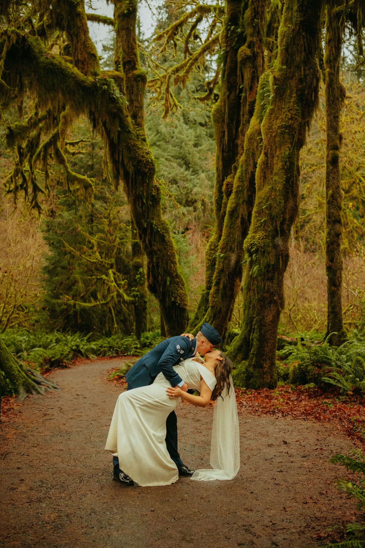 A romantic wedding dip pose on a forest trail surrounded by moss-covered trees.