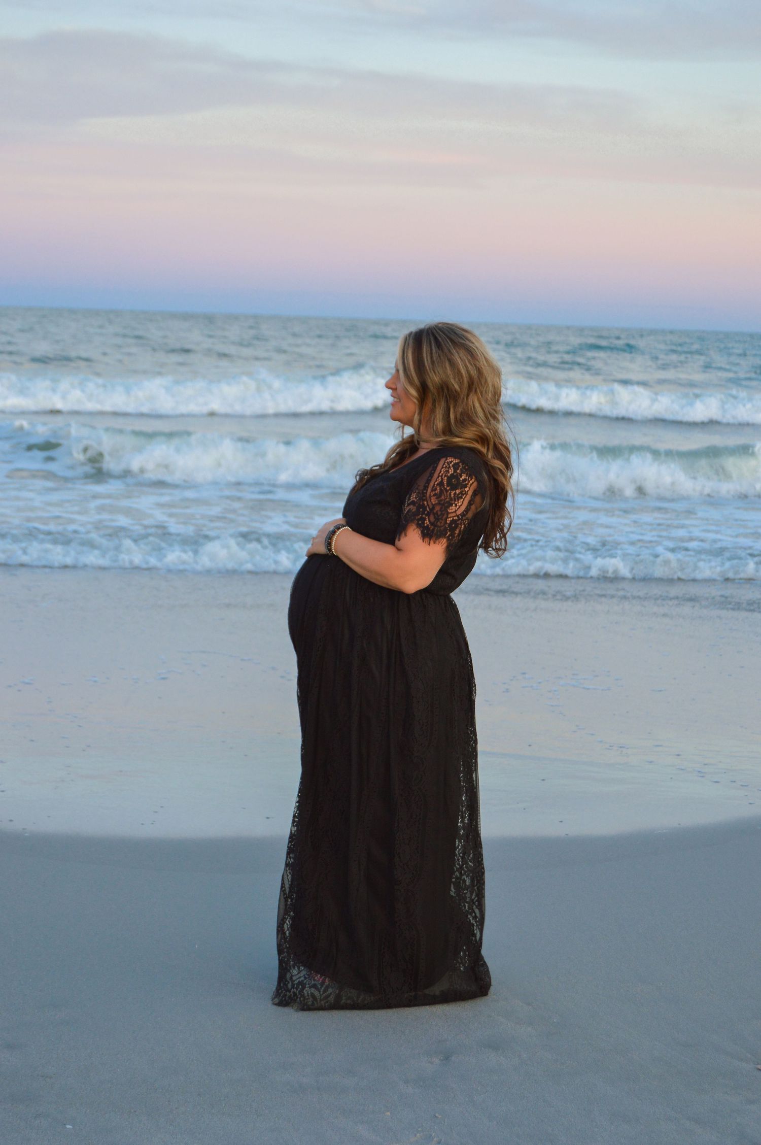woman looking into the distance on the beach in front of the ocean for a maternity session