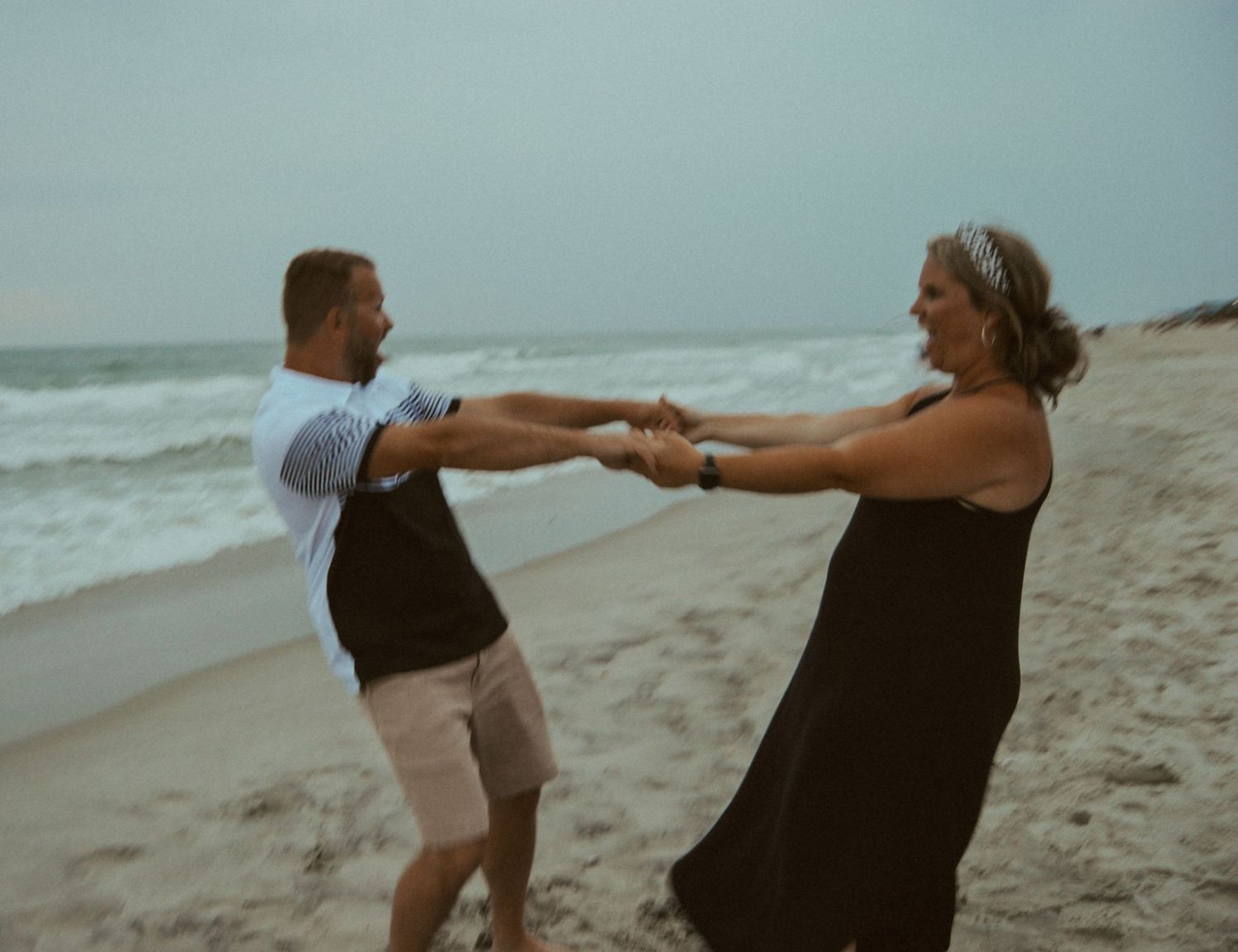 couple twirling each other around on the beach for a photo session