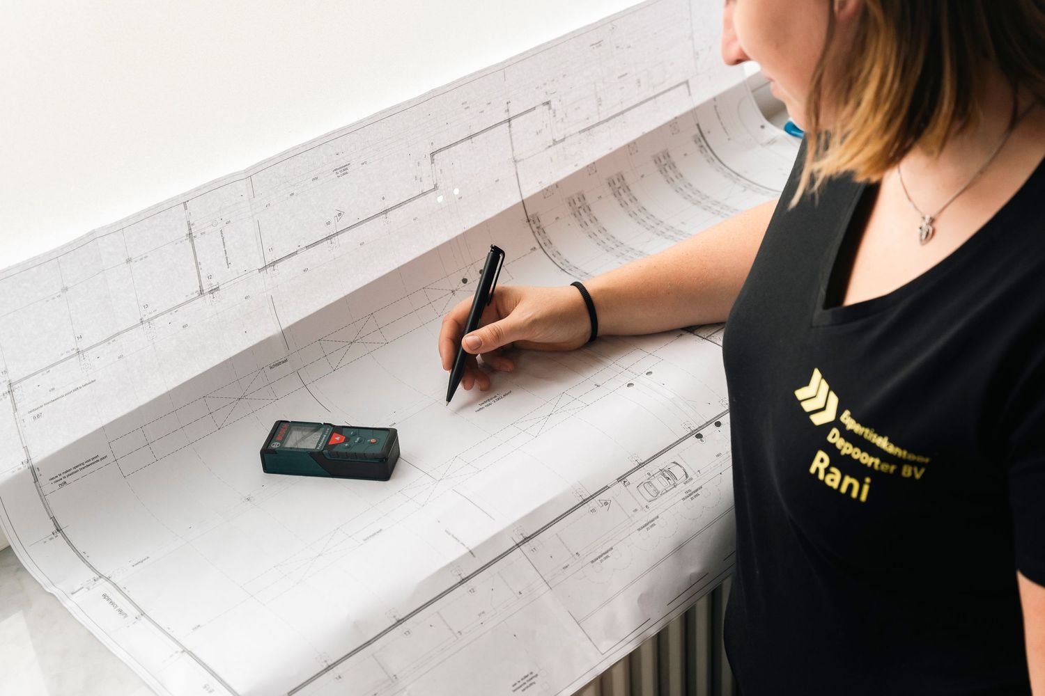 Professional writing on documents at white desk with measurement device nearby.