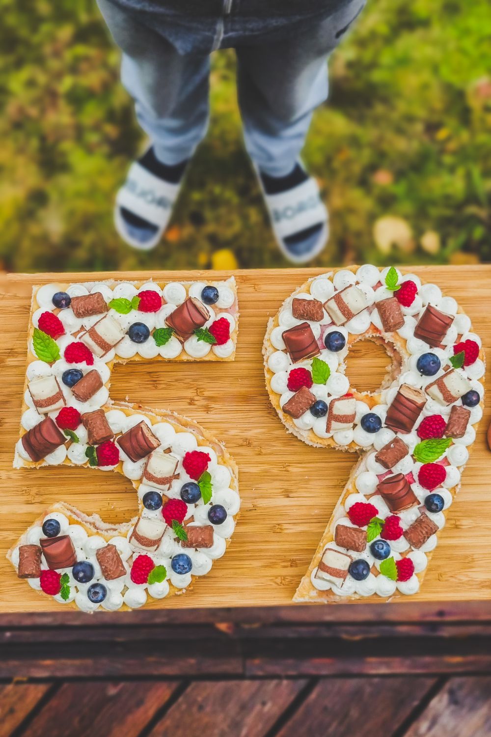 Number-shaped cream cakes decorated with berries, chocolates and candies spelling out '59'.