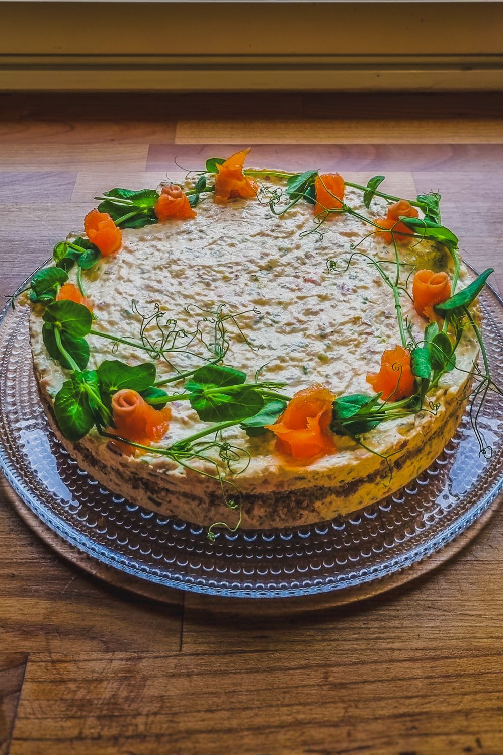 Elegant layered cake decorated with orange carrot decor and green herbs in a circular pattern.