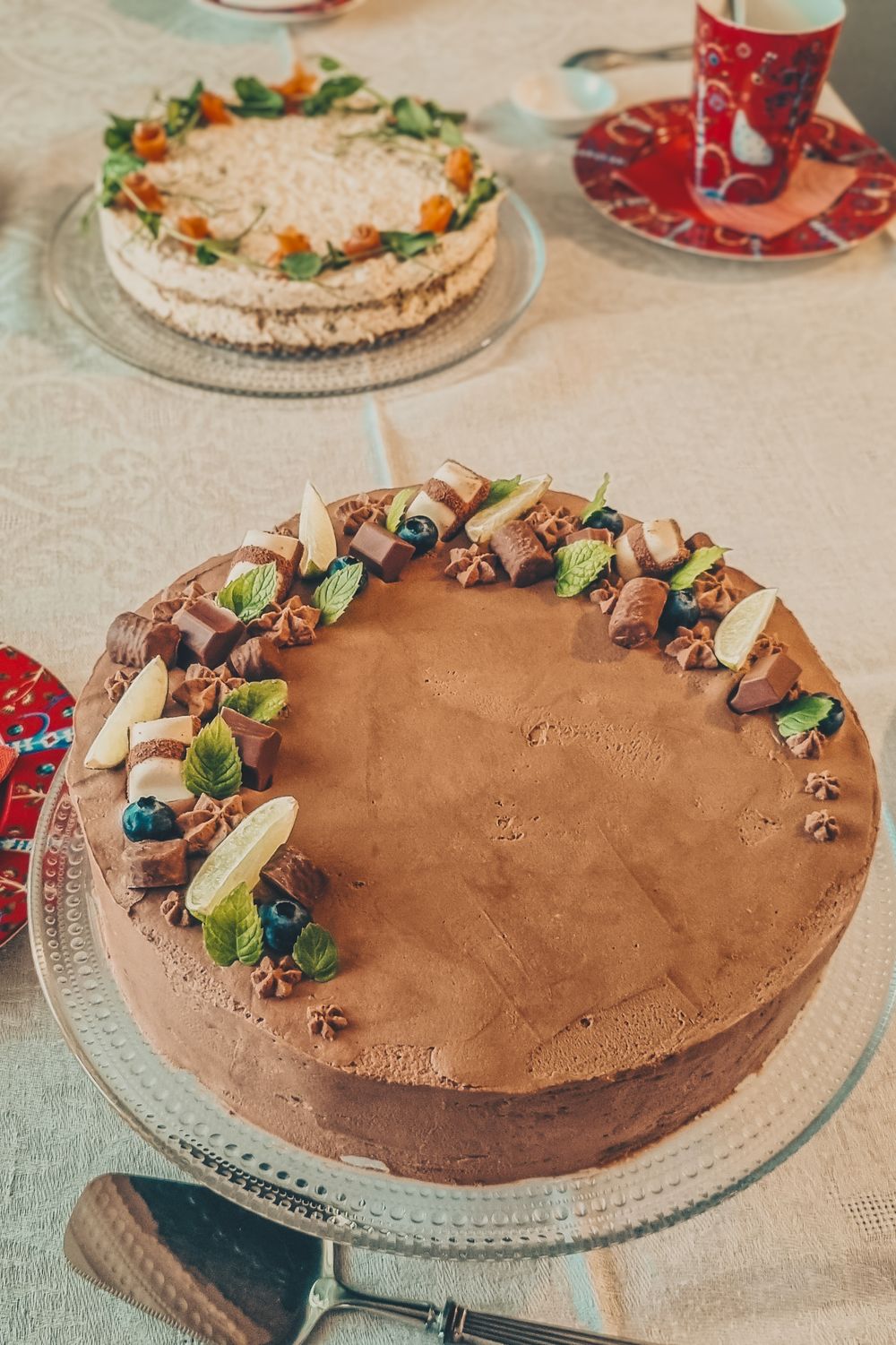 Two cakes on glass plates, one chocolate with decorative toppings and one with orange garnishes.