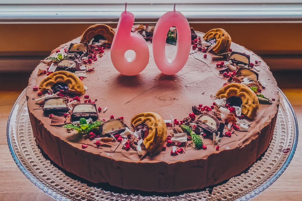 A chocolate birthday cake decorated with pink '60' candles and colorful candy toppings.