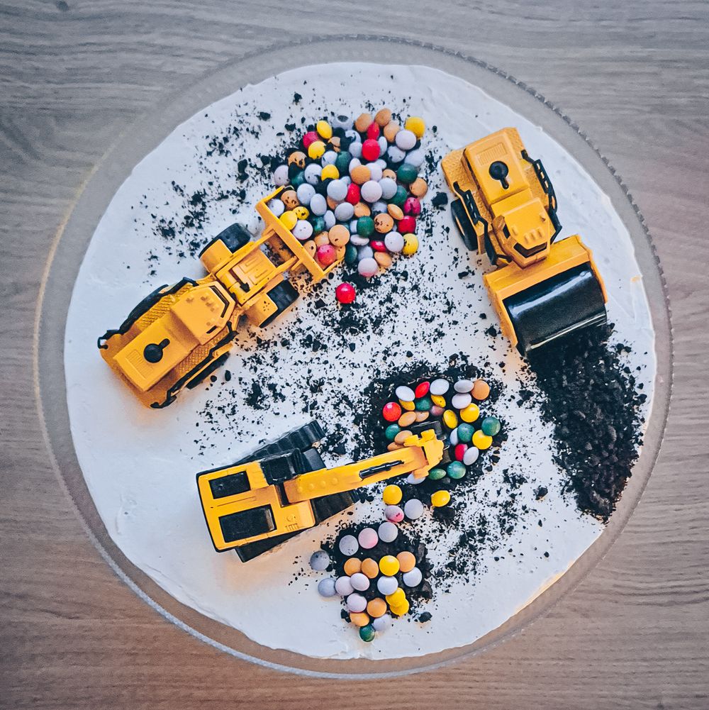 Toy construction vehicles moving colorful candies on a white plate with black sprinkles.