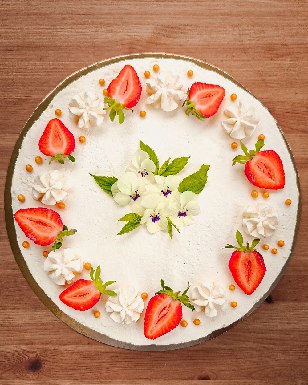 A white frosted cake decorated with fresh strawberry slices and white cream rosettes on a wooden surface.