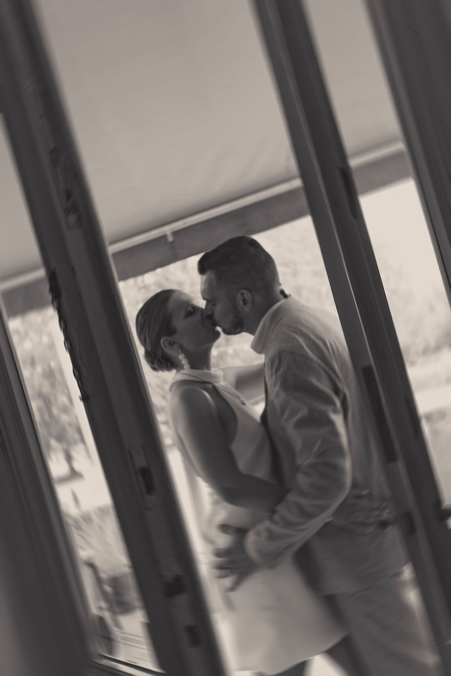 Black and white photo of couple's intimate moment framed through window panes.