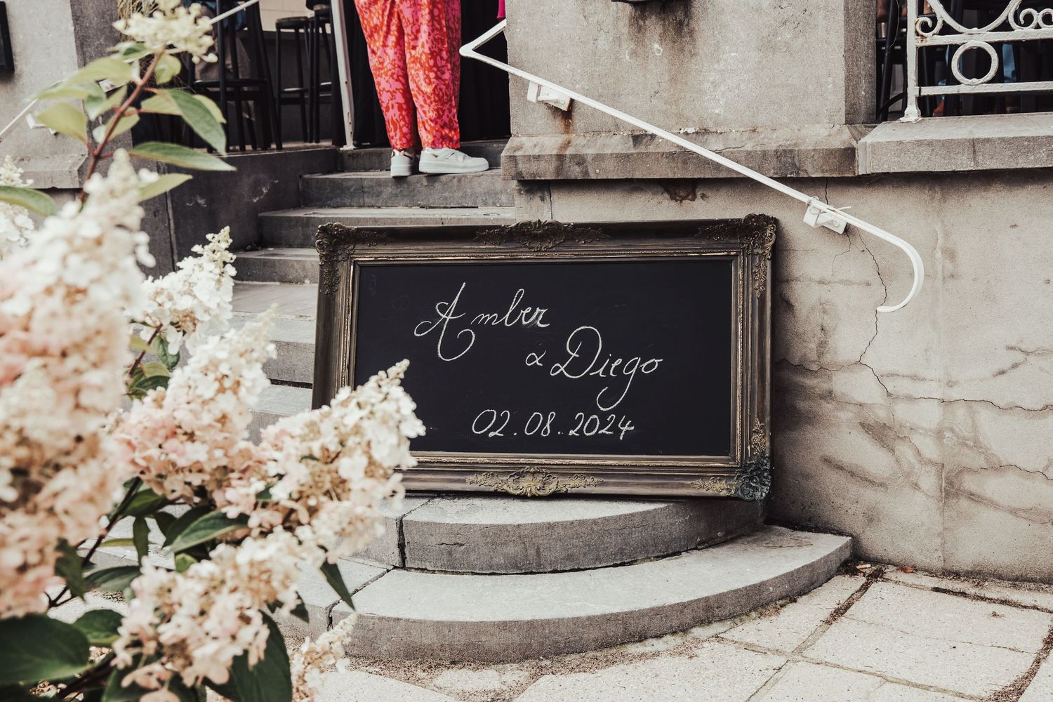 A decorative chalkboard wedding sign with floral arrangements on stone steps.