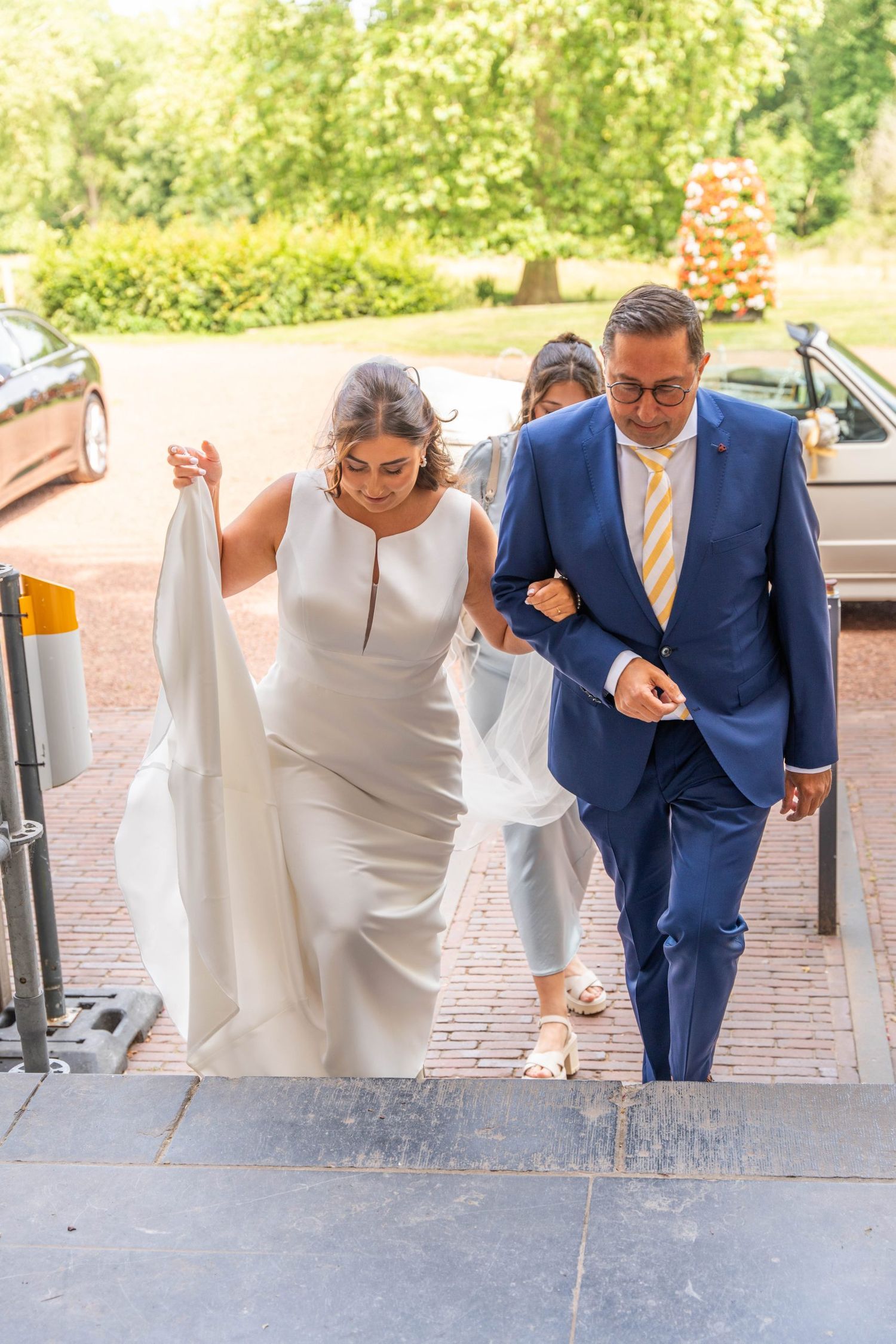 A couple carefully descends stone steps while holding their formal attire.