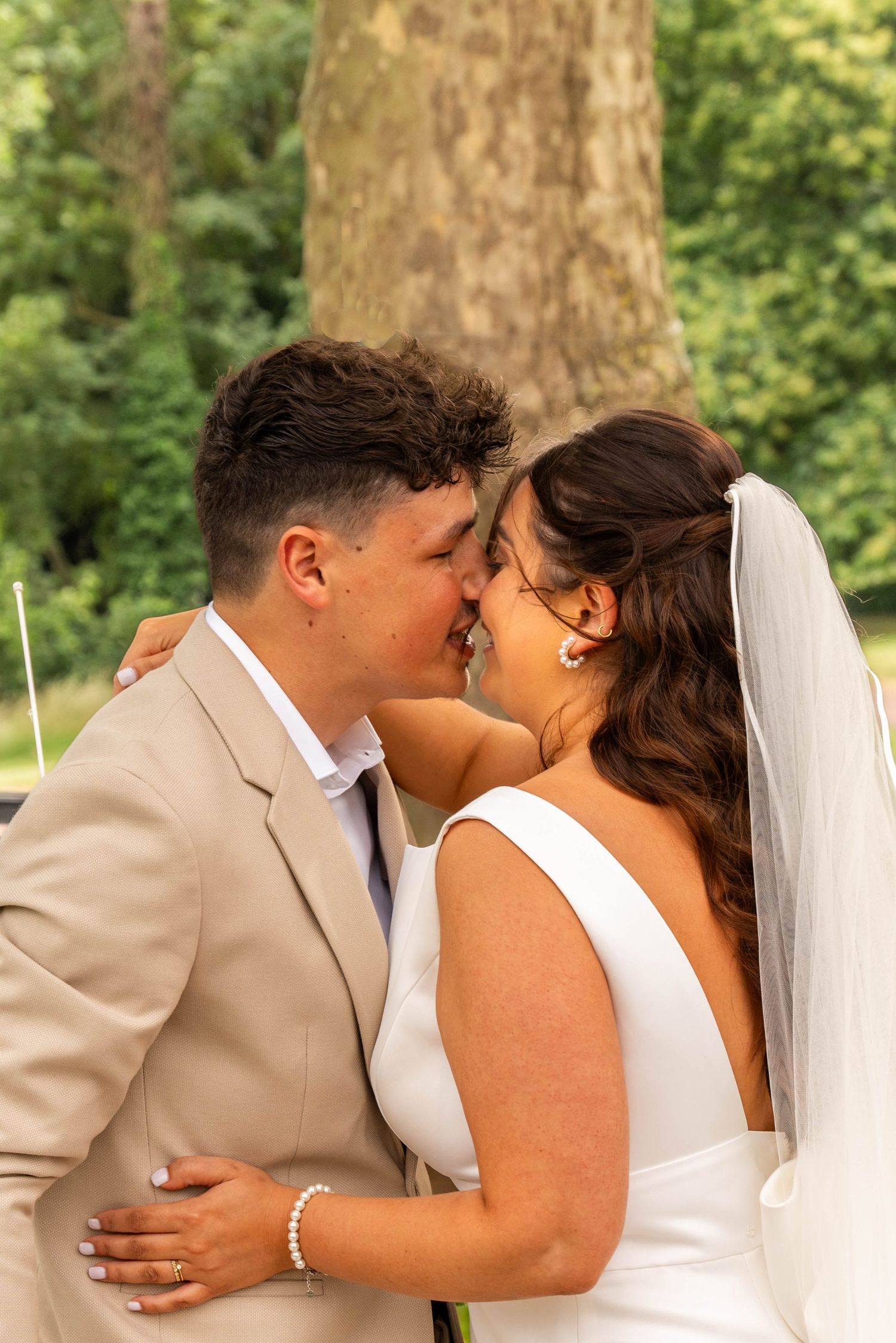 A romantic wedding moment captured between newlyweds under a large tree.