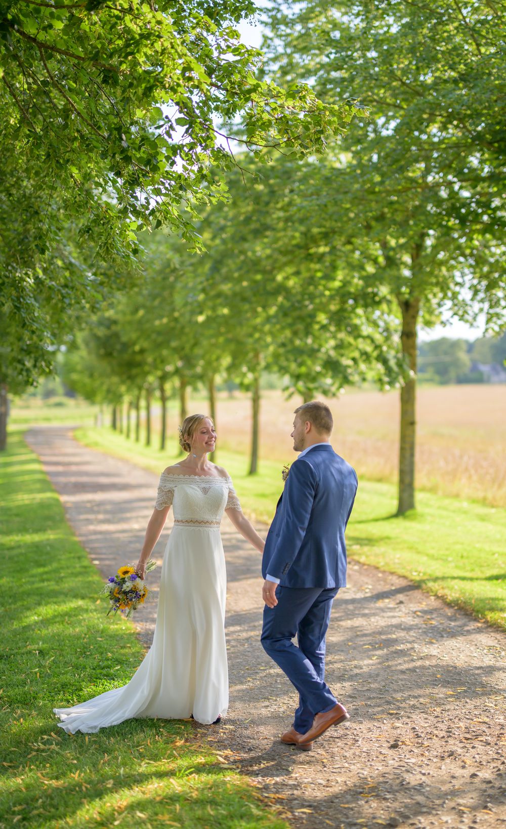 Couple walking along tree-lined path with summer greenery and golden sunlight.