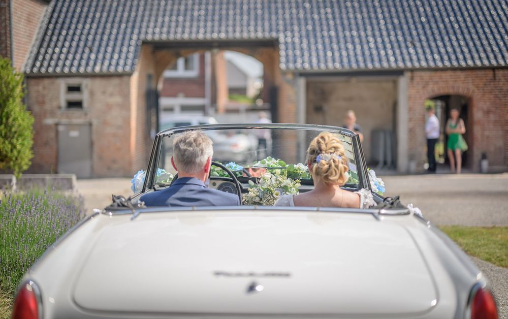 A classic convertible car decorated with wedding flowers and ribbons parked in front of a brick building.
