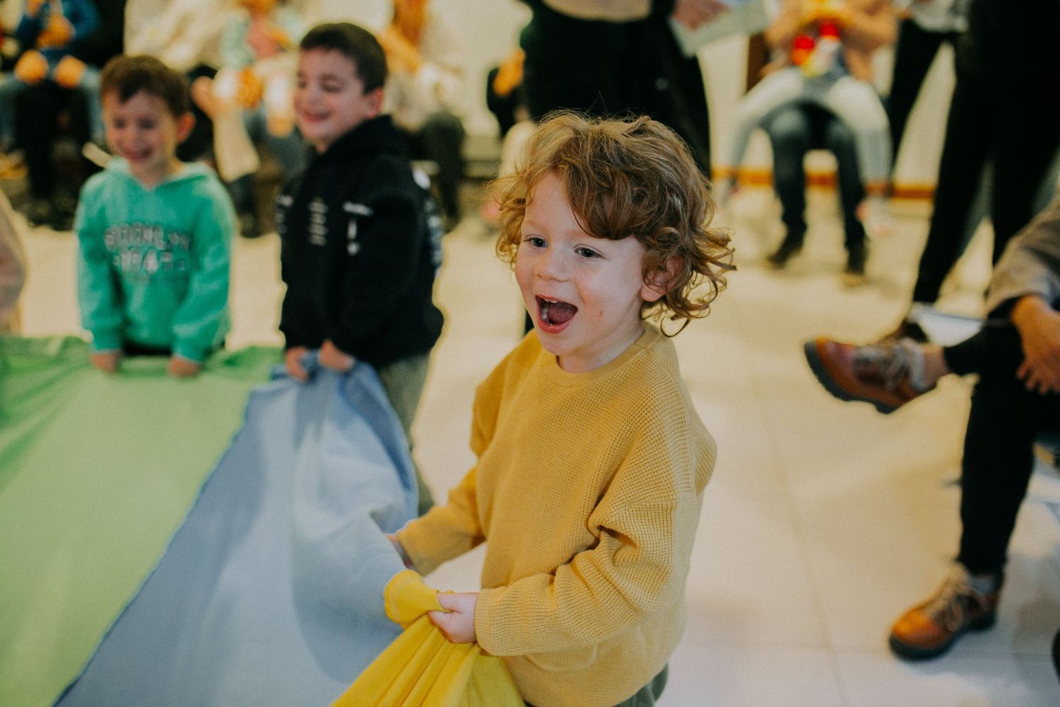 A child in a yellow sweater laughing and having fun at an indoor party.