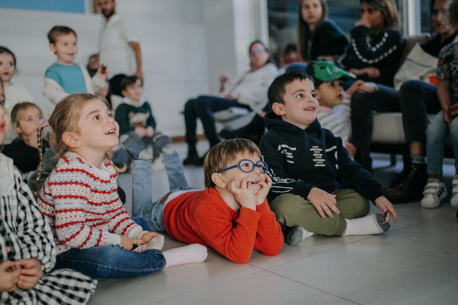Children sitting on the floor watching entertainment at an indoor party event.