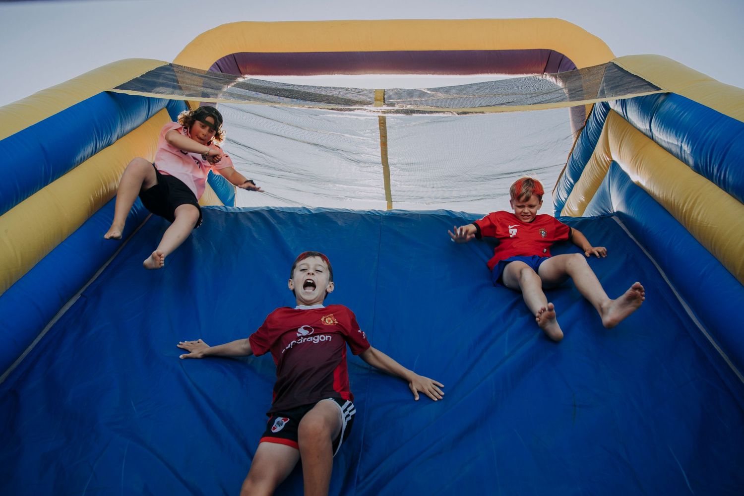 Three people lay relaxed on a large inflatable bounce house with blue and yellow colors.