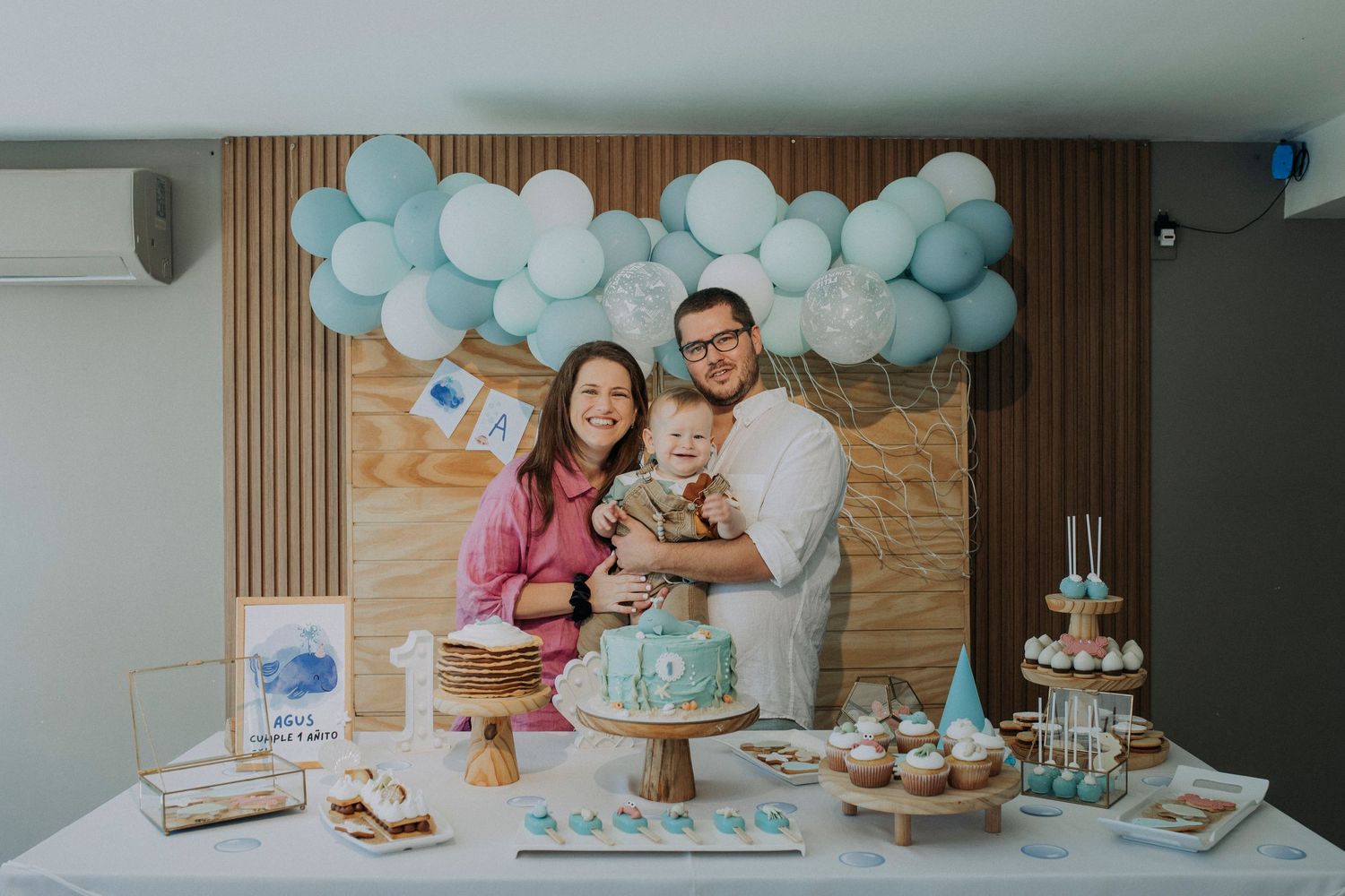 A festive dessert table decorated with blue and white balloons features a birthday cake and treats at a celebration.