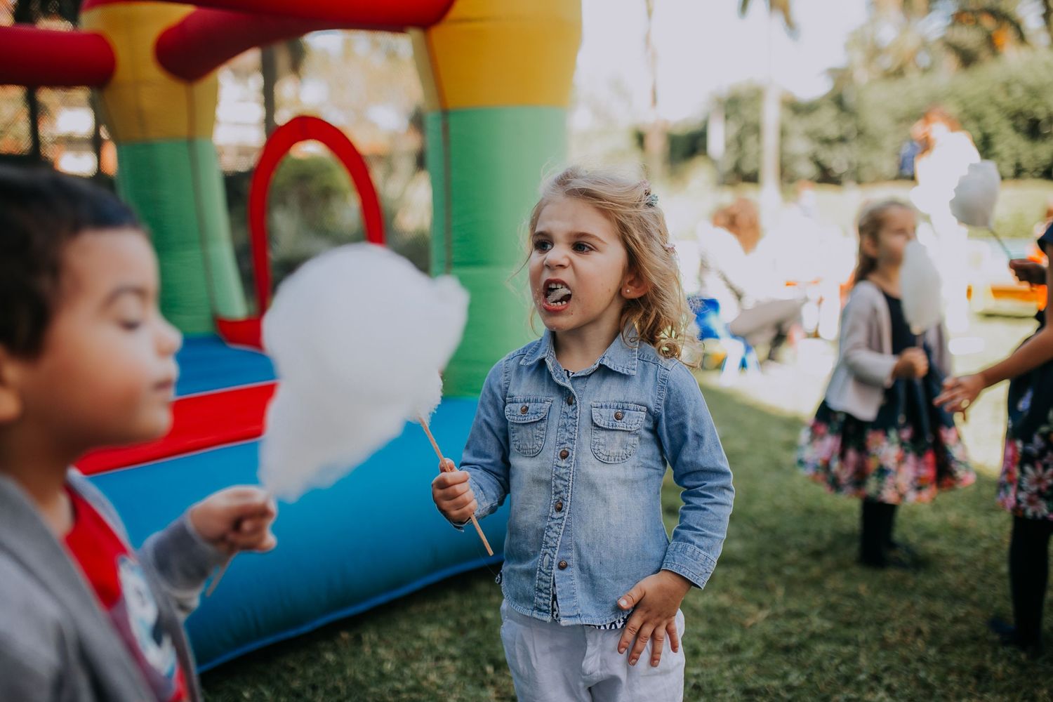 A child in a denim jacket expressing excitement near a colorful bounce house at a party.