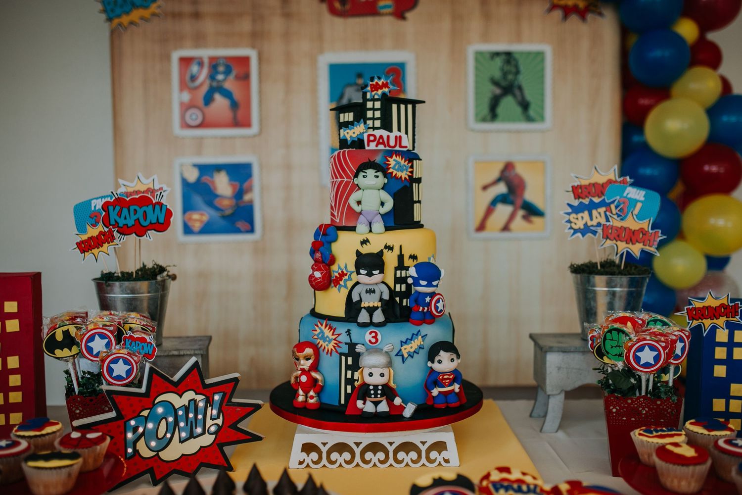 A superhero themed birthday cake with multiple tiers decorated in comic book style with colorful patterns and decorations.