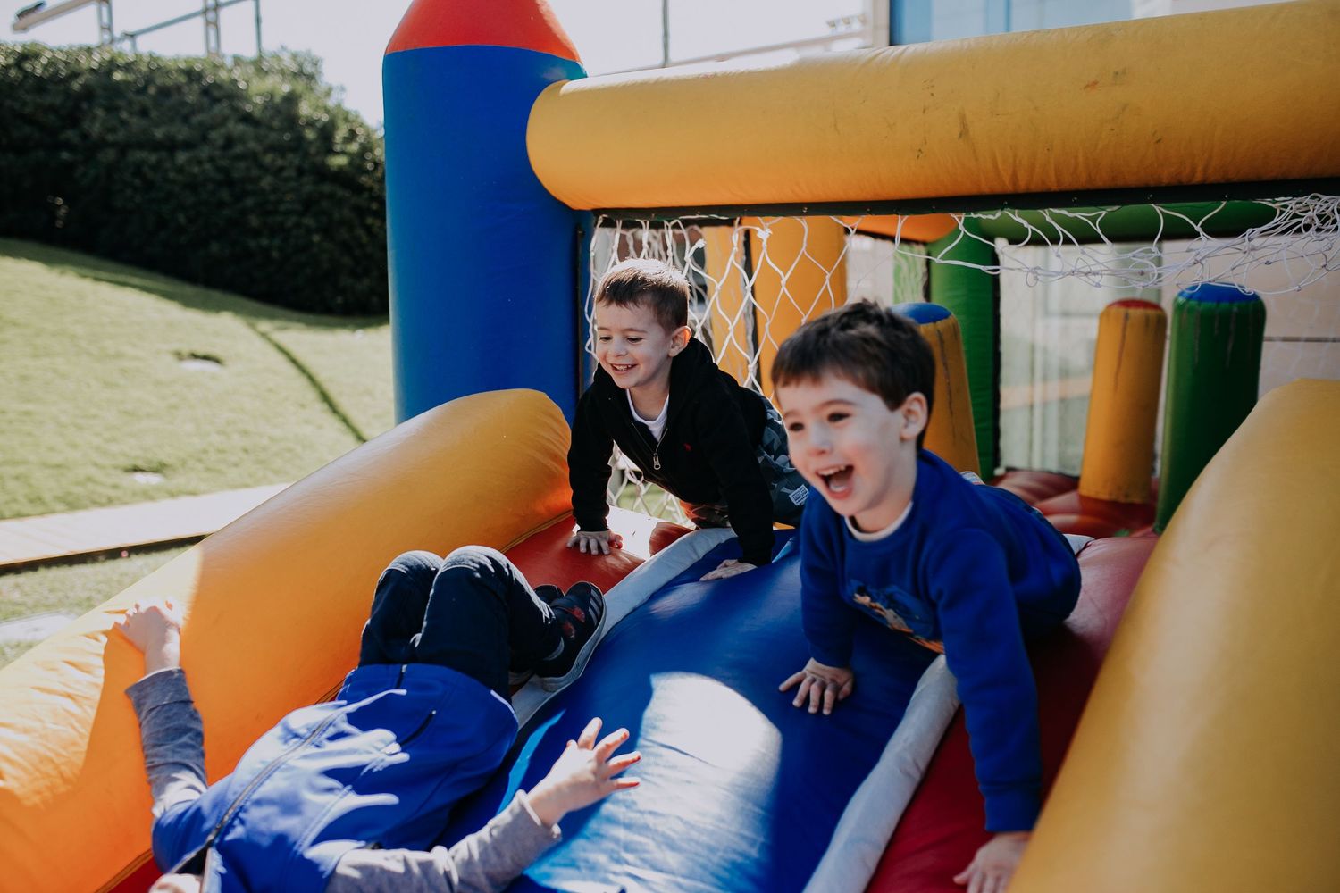Children having fun sliding down an orange and blue inflatable bounce house slide.
