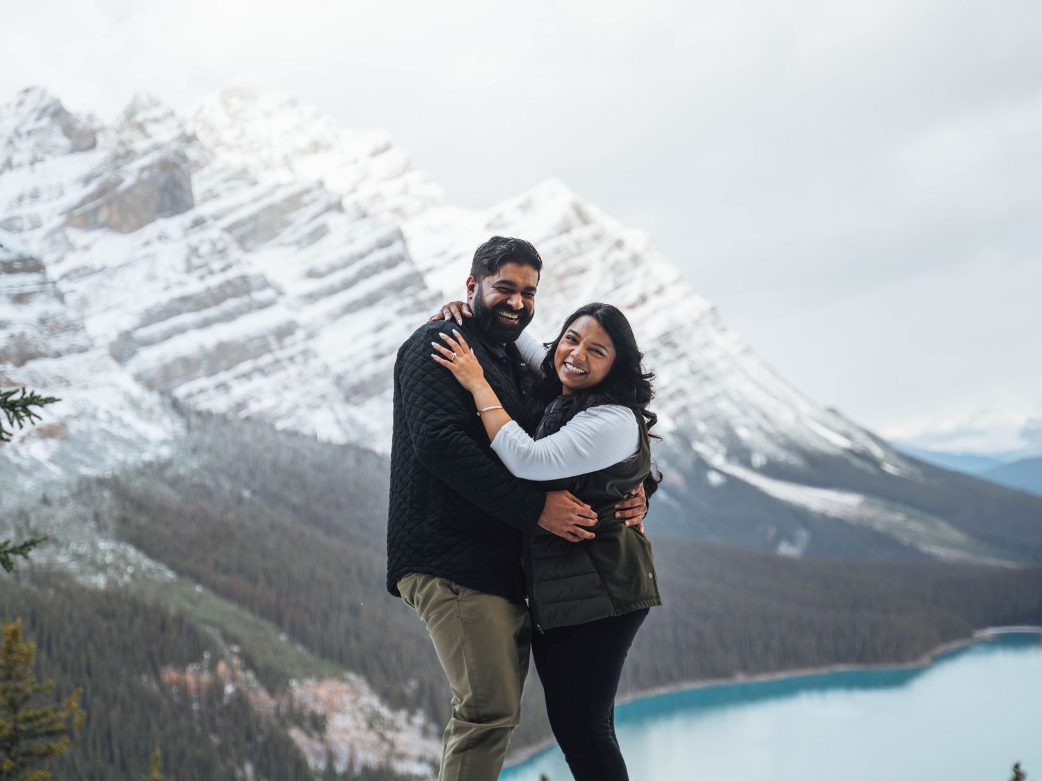 Couple cuddles with a mountainside in the Rockies in the backdrop. Banff engagement photography.